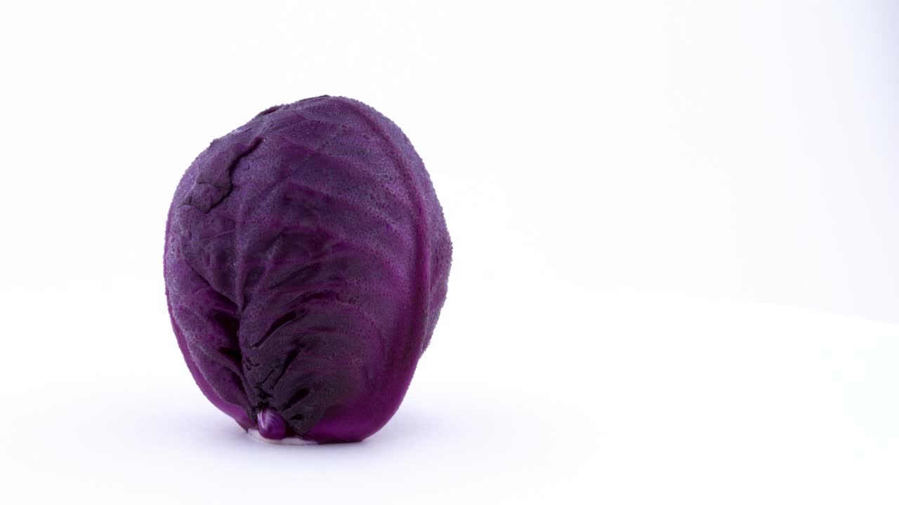 la mitad del marco de un mini repollo púrpura entero con gotas de agua está girando en la mesa giratoria aislada en el fondo blanco. primer plano. macro.