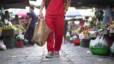 a vibrant street market scene showcasing a person in red attire walking with a bag, surrounded by fresh produce, emphasizing the bustling atmosphere of local shopping