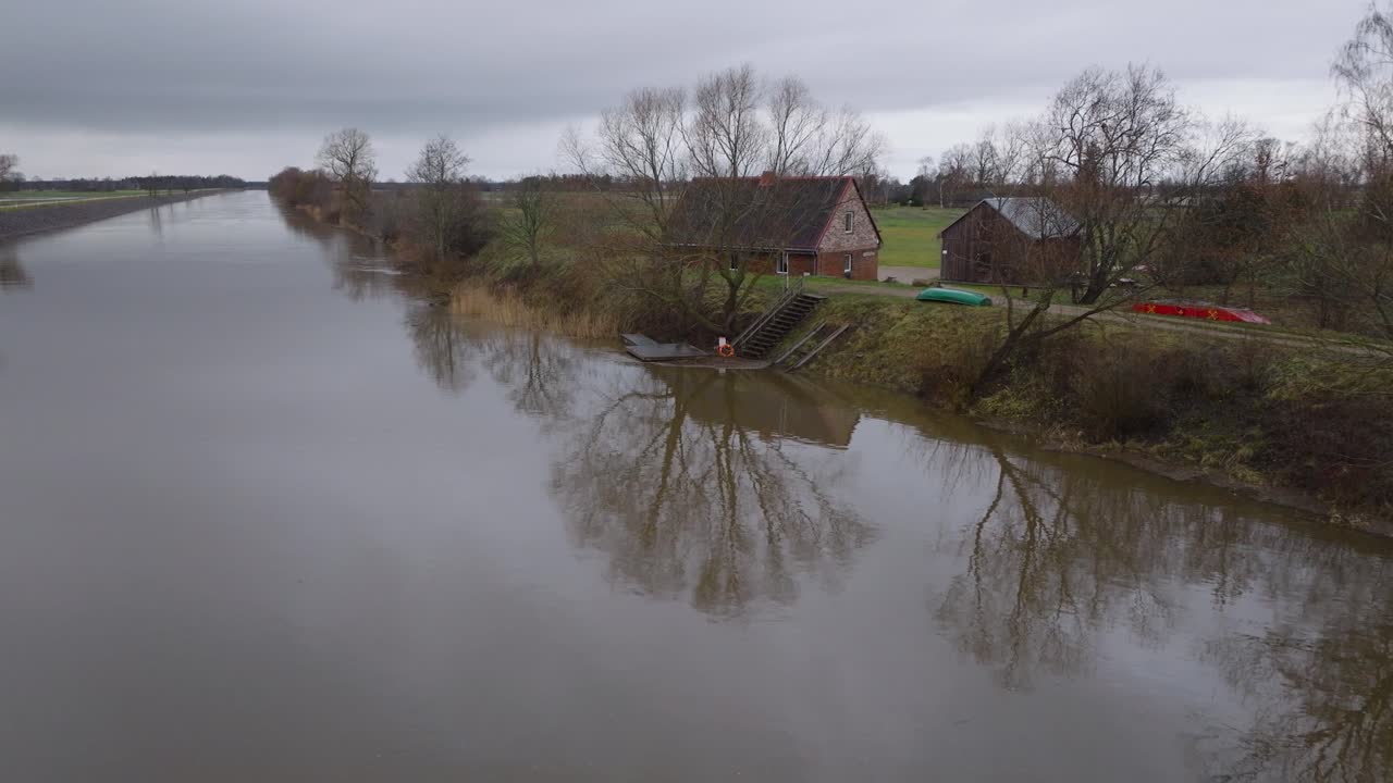 Etablerende luftfoto af høj vandstand om foråret, oversvømmelse af Barta-floden, brunt og mudret vand, overskyet dag, afsidesliggende hus ved flodbredden, bred droneoptagelse der bevæger sig lavt fremad