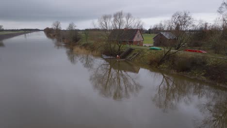 aerial establishing view of high water in springtime, barta river flood, brown and muddy water, overcast day, remote house on the bank of the river, wide drone shot moving forward low