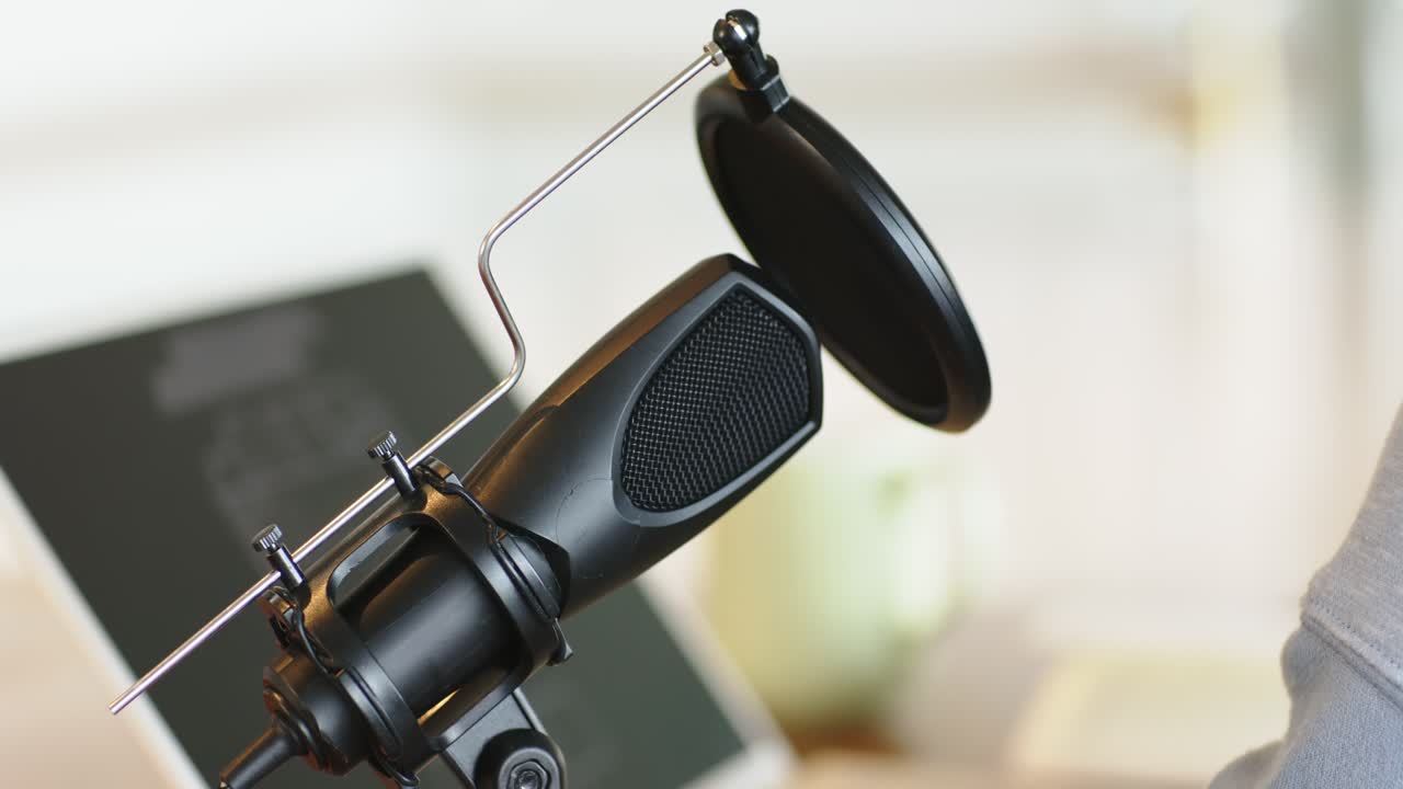 Adult entering frame and adjusting pop filter on microphone to prepare for recording and speaking