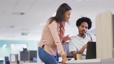 Video-of-happy-diverse-businesswoman-and-businessman-using-laptop-and-talking