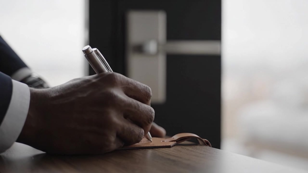 A Close-Up View of Hands Writing with a Pen on a Tag Near a Door Handle, Captured in a Modern Indoor Setting with Natural Light Streaming In
