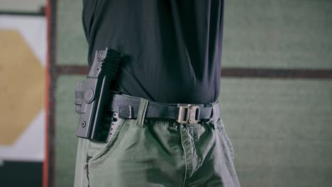 primer plano de un instructor de tiro sacando una pistola de su funda en un campo de entrenamiento cubierto