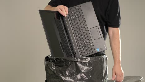 a man is throwing away a used and broken laptop into the trash bin