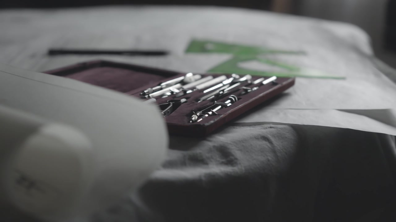 Camera side slide shows an assortment of classic manual drafting tools resting on a desktop covered with technical blueprint sheets. Perfect for engineering, real estate, and design context.