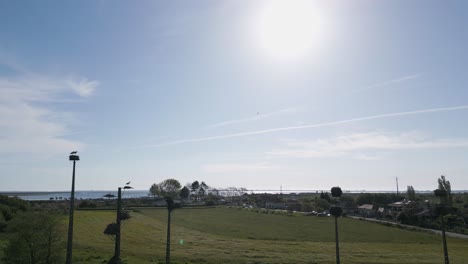 Störche-Im-Flug-Und-Nisten-Auf-Stangen-Vor-Einem-Sonnenbeschienenen-Himmel-In-Murtosa,-Aveiro,-Portugal---Luftaufnahme