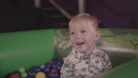 a young boy plays in ball pit and throws balls around whilst smiling - ungraded