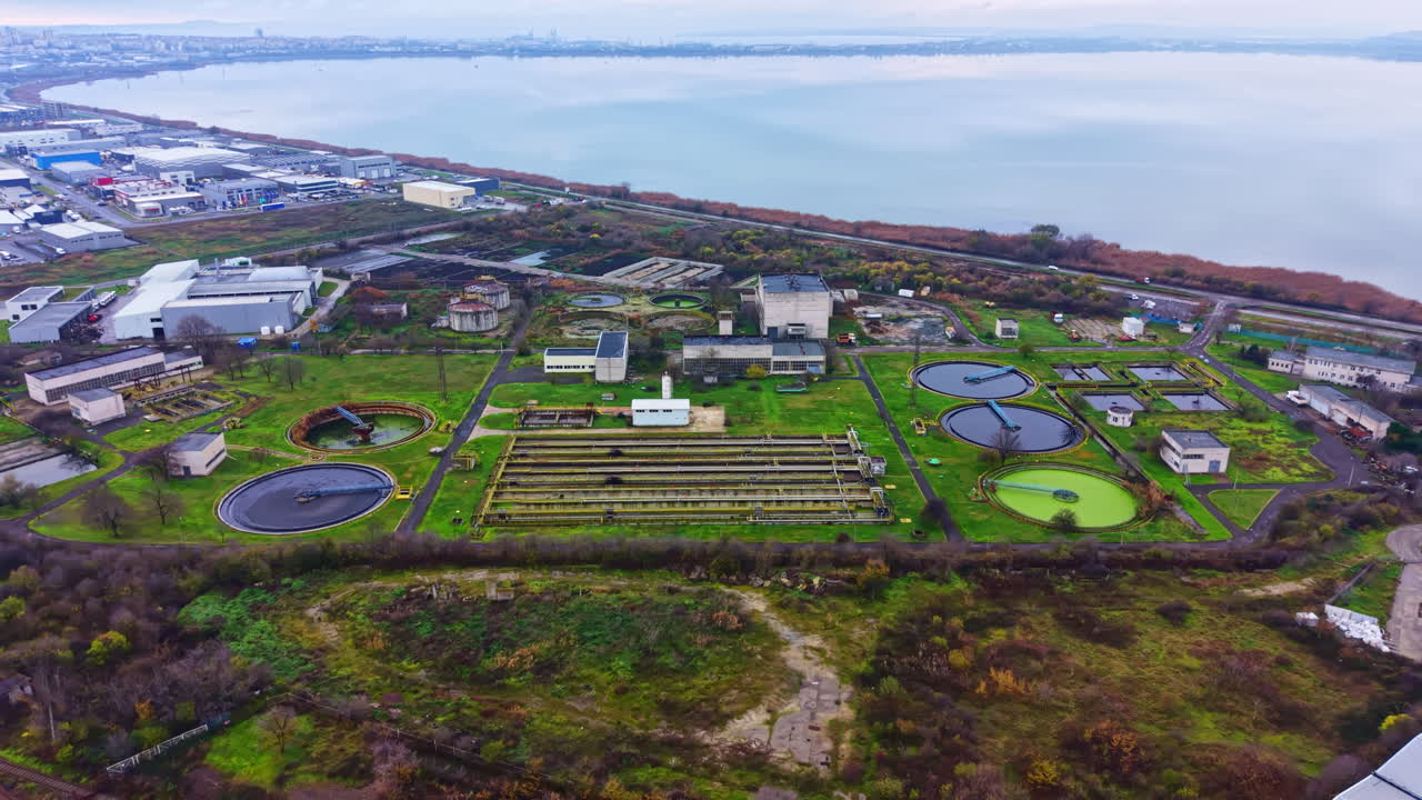 Water treatment facility located near a large body of water with various tanks and buildings during an overcast day