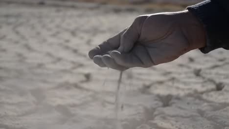 a man's hand gathers soil from an arid landscape, capturing the essence of drought and environmental change in a desolate setting