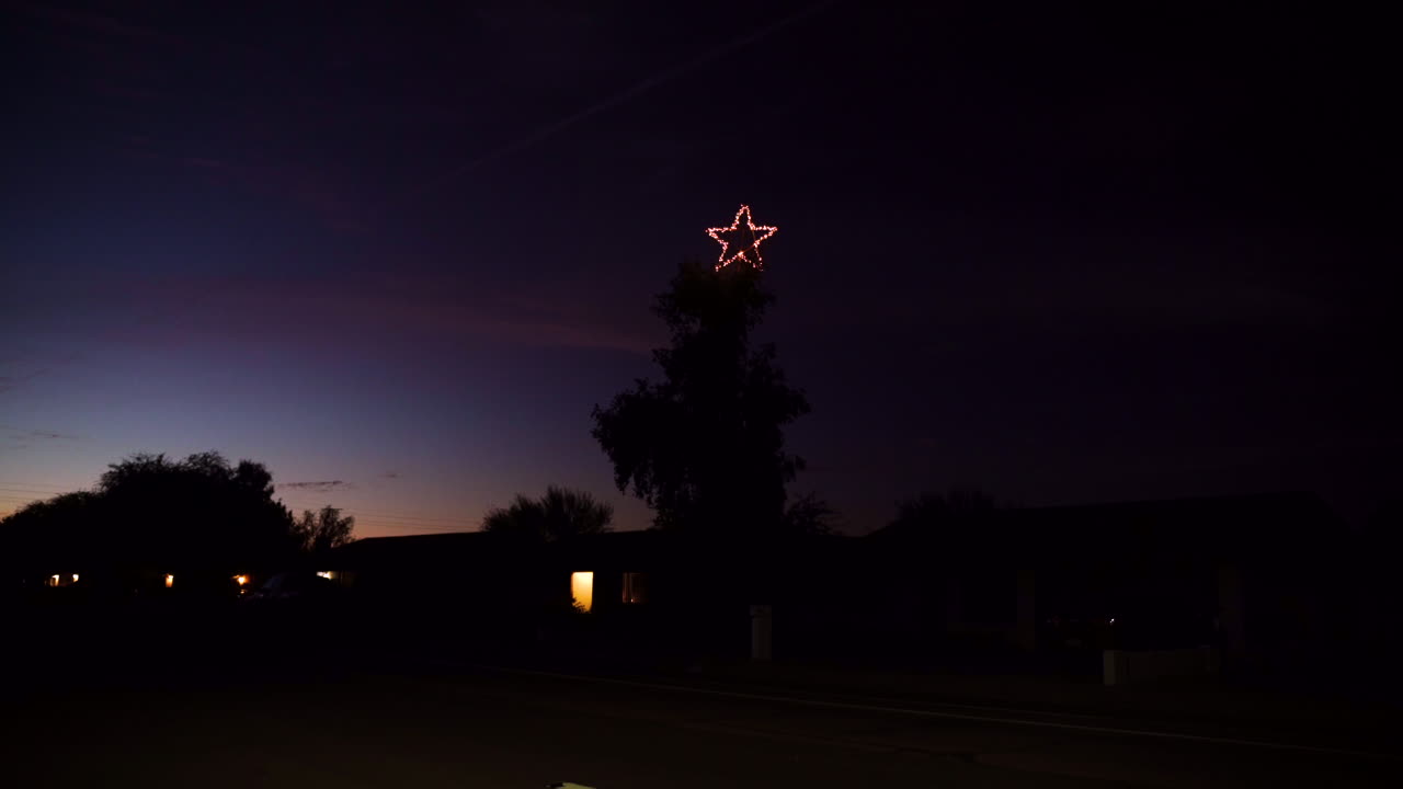 Grande estrela de Natal em uma árvore grande à noite, à beira da estrada com um carro.