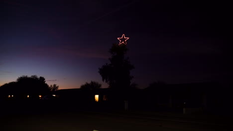gran estrella de navidad en un árbol grande por la noche al lado de la carretera con el coche