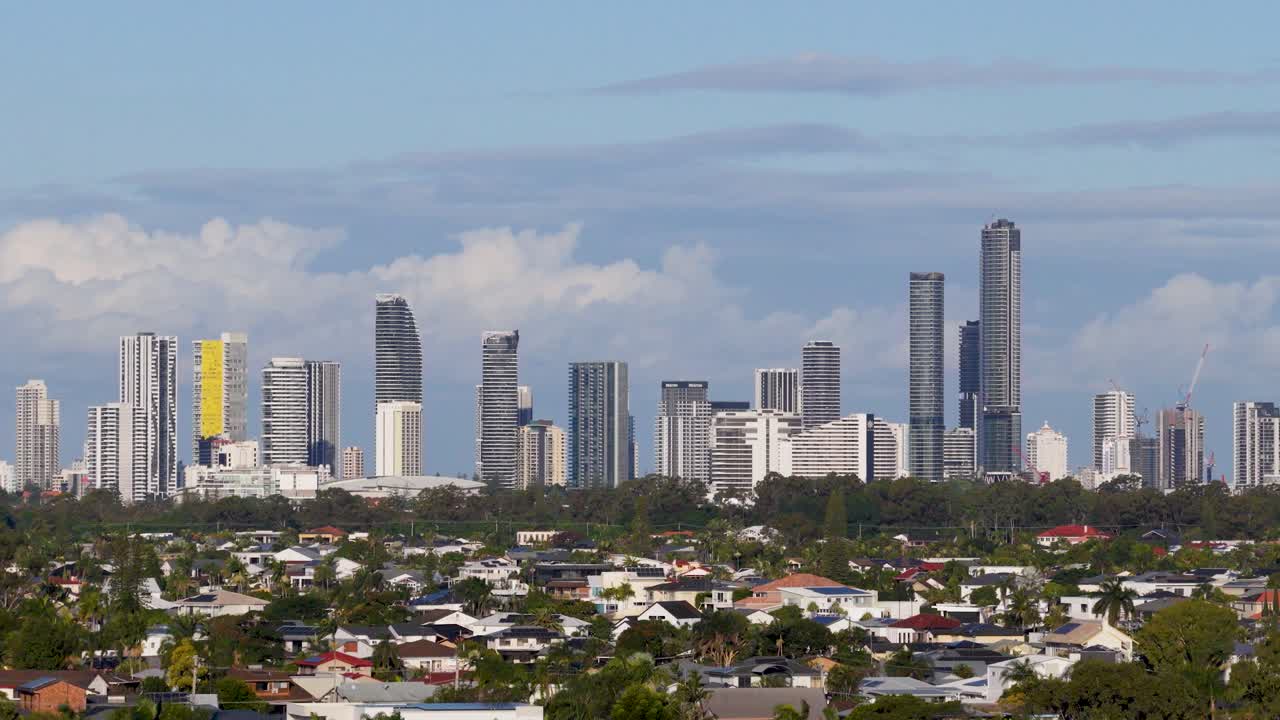 Drone footage captures Gold Coast skyline with lush greenery and golf course in foreground under clear blue skies