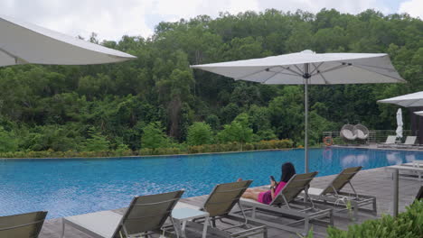 huésped del hotel en una silla de sol usando el teléfono móvil junto a la piscina