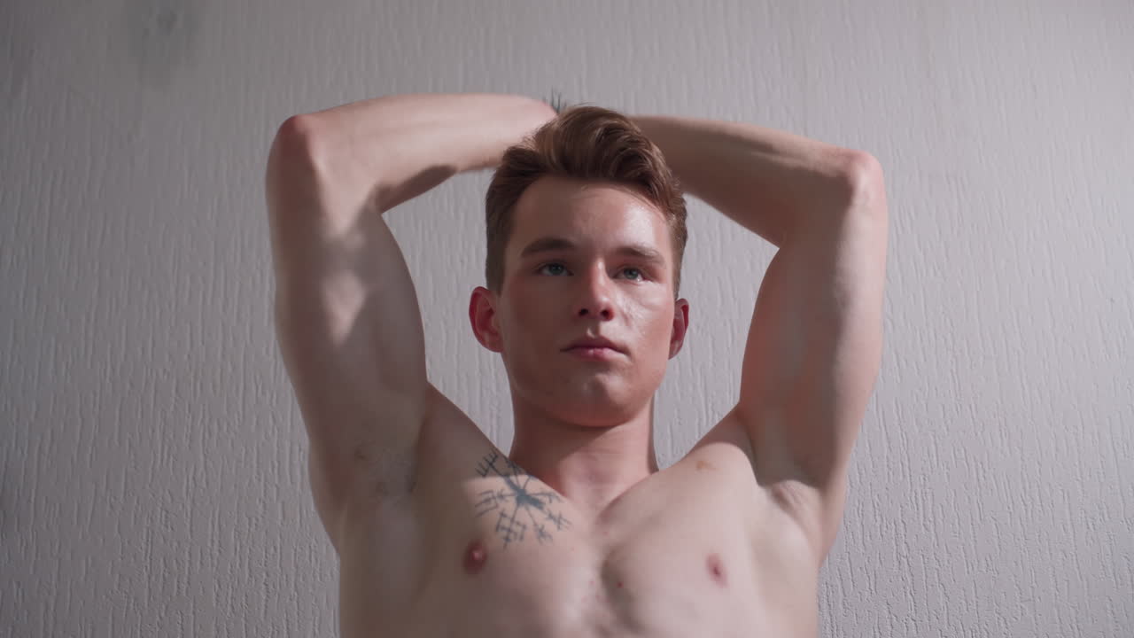 gym lover standing with arms raised, pulling resistance rope behind back, displaying toned torso and defined abs, positioned near window with soft light casting subtle shadows on muscular body