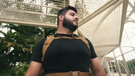 joven viajero masculino con mochila tomando un respiro dentro de un invernadero tiro orbital a cámara lenta