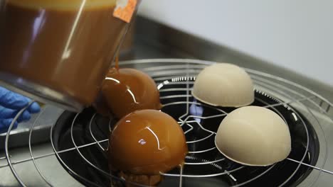 unrecognizable confectioner covers baked cakes with caramel glazing. process of preparing delicious dessert. close-up footage.