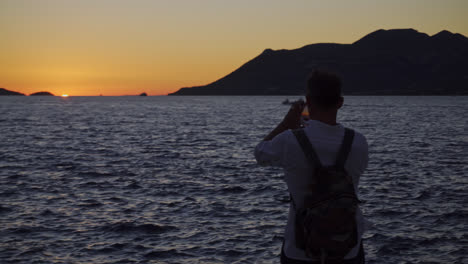 backview of a man taking photos of the sea during sunset. - medium, rear