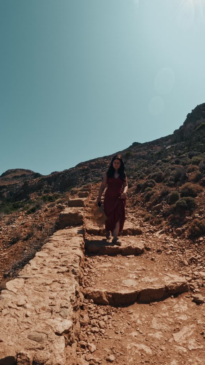 A Lady Walks Down a Rocky Path Under the Bright Sun at Balos Beach in Crete, Chania, Greece - Vertical Shot
