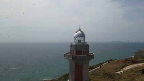 Drone-orbits-around-Faro-de-Punta-Ballena,-famous-lighthouse-in-Porlamar,-Margarita-Island,-revealing-the-Caribbean-Sea,-birds,-coastal-buildings,-hotels-and-resorts,-marshy-body-of-water,-Venezuela