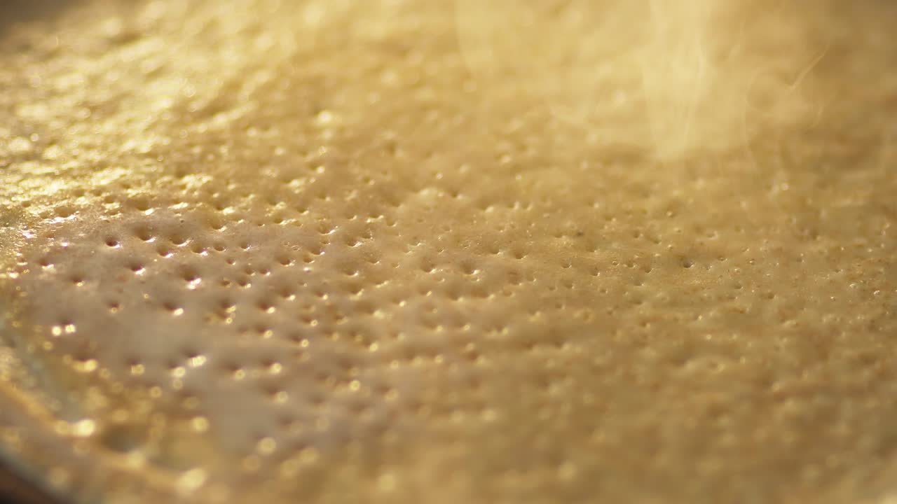 video de 4k. freír panqueque en la sartén de primer plano. la bruma perfumada se eleva durante la preparación de una comida deliciosa