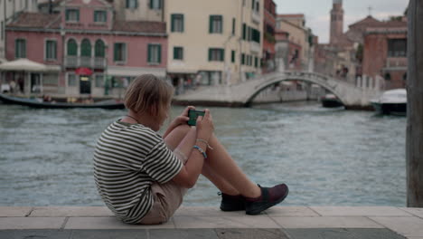 teenager playing on phone by venice canal