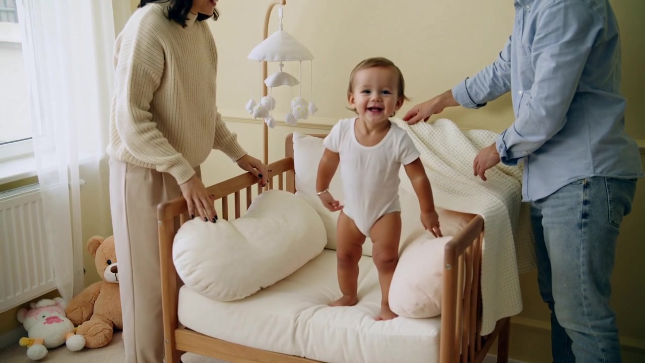 Posizionando il cuscino, stendendo la coperta, genitori che rifanno il letto nella cameretta mentre il neonato è in piedi, seduto nella culla