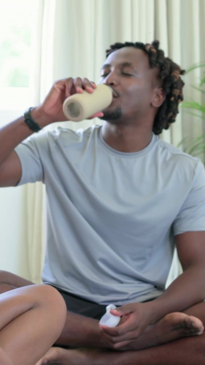 Vertical video: Man taking bottle handed at home, opening beige bottle, drinking, sharing in tee