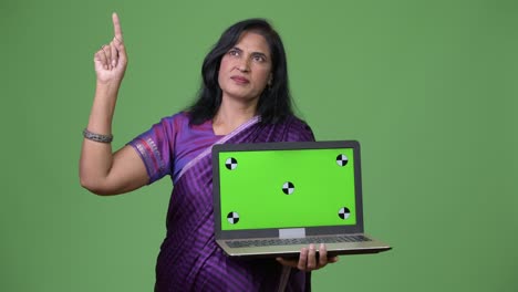 mature beautiful indian woman thinking while showing laptop and pointing up