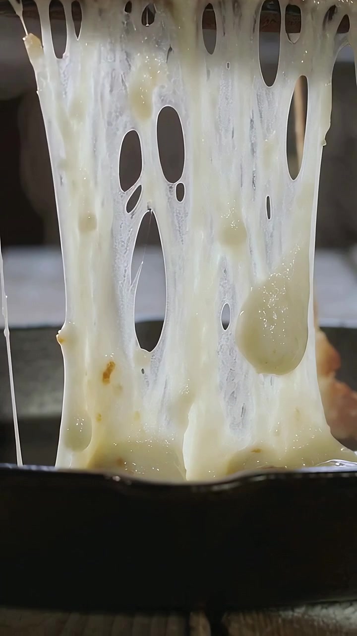 Vertical video: Lifting hand stretching melted cheese from round rolls in kitchen pan, wood board