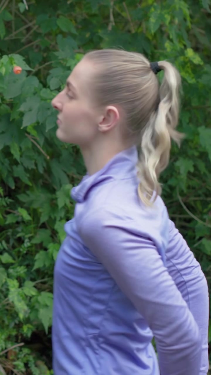 Video verticale: Mani alzate, donna che si lega la coda di cavallo al parco per allenarsi, top color lavanda, elastico per capelli