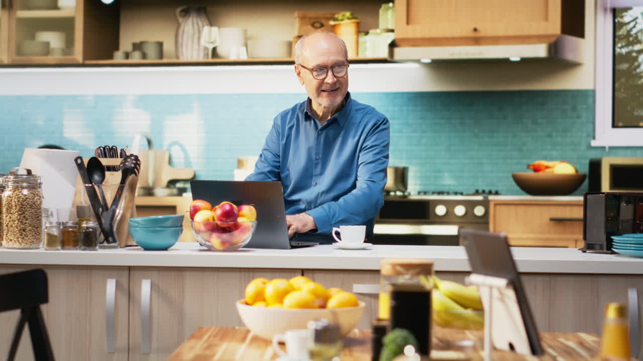 Senior adult in calm kitchen setting scrolling apps on her laptop
