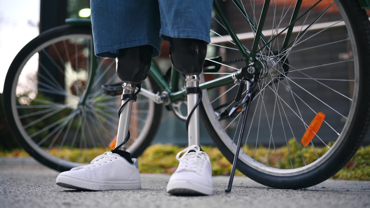 View of a man with prosthetic legs. Putting the bike on the kickstand and standing next to it