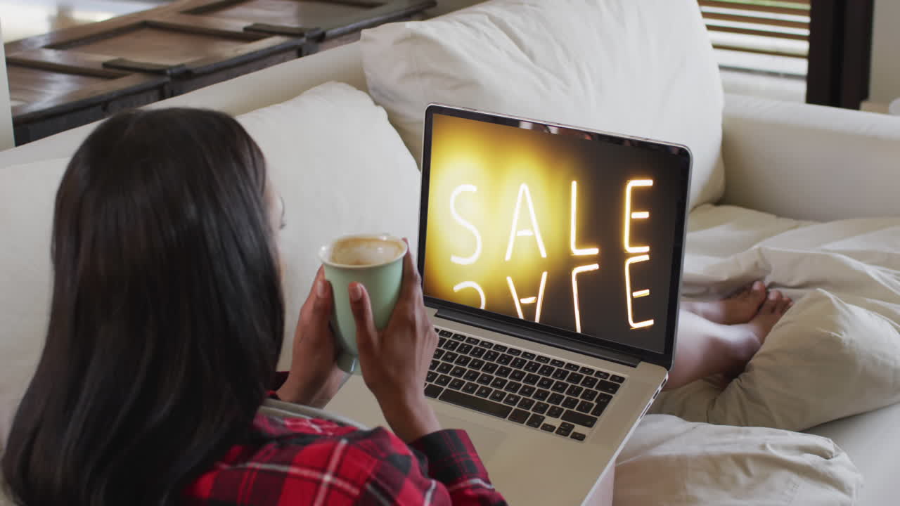 mujer biracial en el sofá con café, usando portátil para comprar en línea, cámara lenta