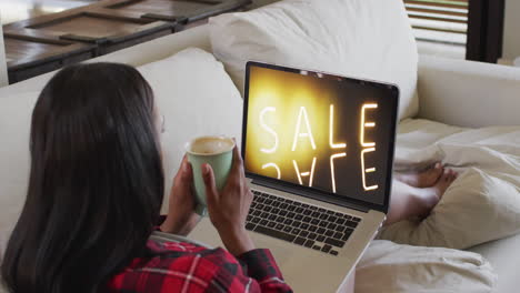 Biracial-woman-on-couch-with-coffee,-using-laptop-for-online-shopping,-slow-motion