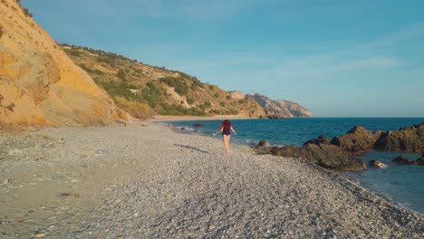 Woman-walking-at-the-beach,-drone-moving-backwards