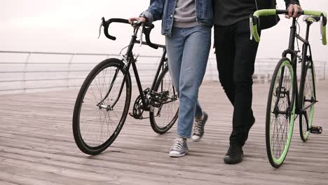 Moderna-Pareja-Joven-Hipster-Caminando-Junto-Con-Sus-Bicicletas-Cerca-Del-Mar-En-El-Día-De-Otoño-Abrazando