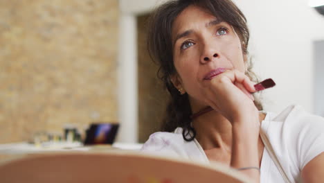 una mujer biracial reflexiona sobre su pintura en casa.
