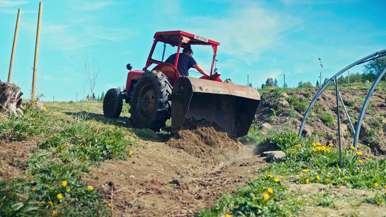 Um homem opera um trator vermelho enquanto trabalha num campo agrícola na Noruega rural