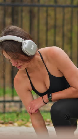 side view of young girl stretching her legs outdoors, close to iron fence while listening to music with headphones, fitness lifestyle captured with a focus on stretching and wellness