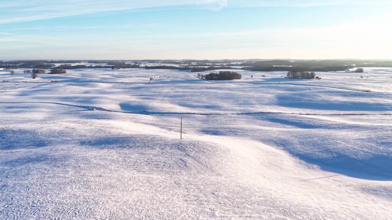 Drone video captures vast snow-blanketed countryside at sunrise, showing undulating terrain, powdery drifts, and tranquil winter scenery in beautiful natural light. No people visible.