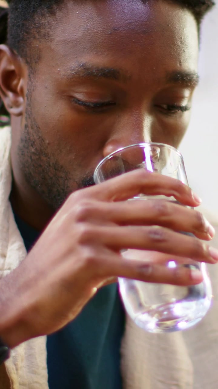 Vidéo verticale : Bras se déplaçant, homme en chemise beige prenant un verre à table, buvant de l'eau et montrant sa montre.