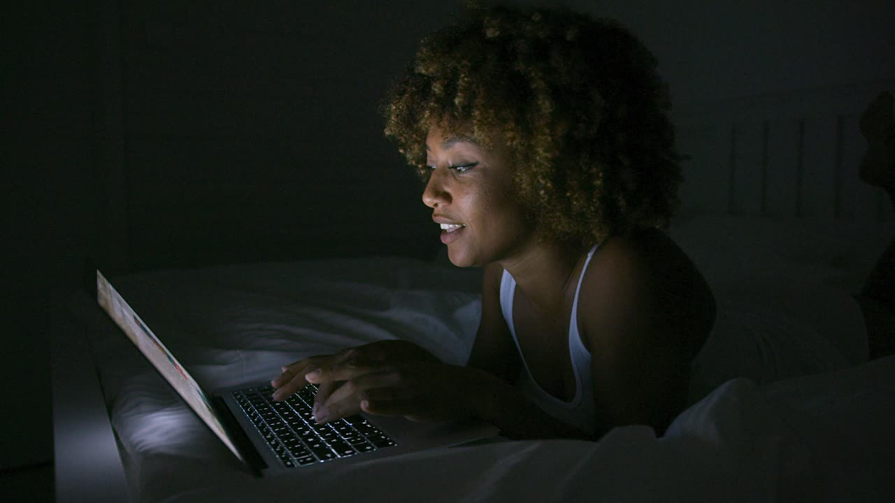 Smiling woman chatting with laptop in dark