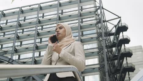 muslim businesswoman on mobile phone standing outside office in city 1