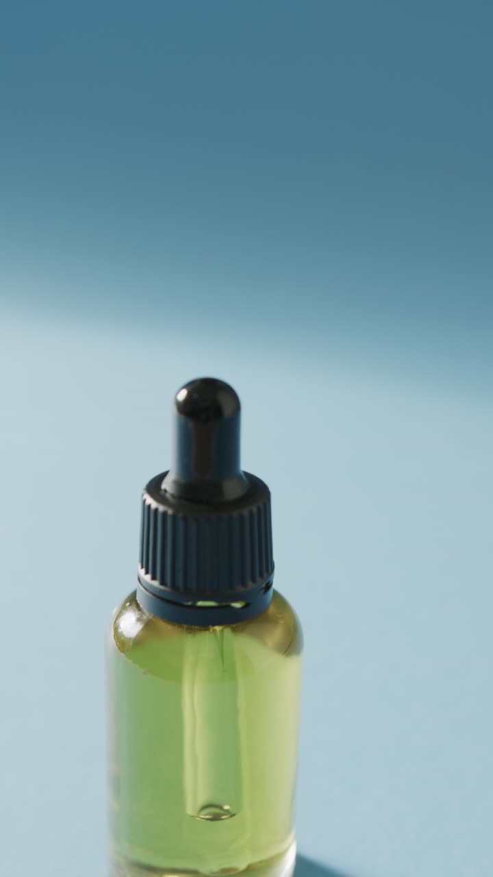 Vertical video of close up of glass bottle with pump and copy space on blue background