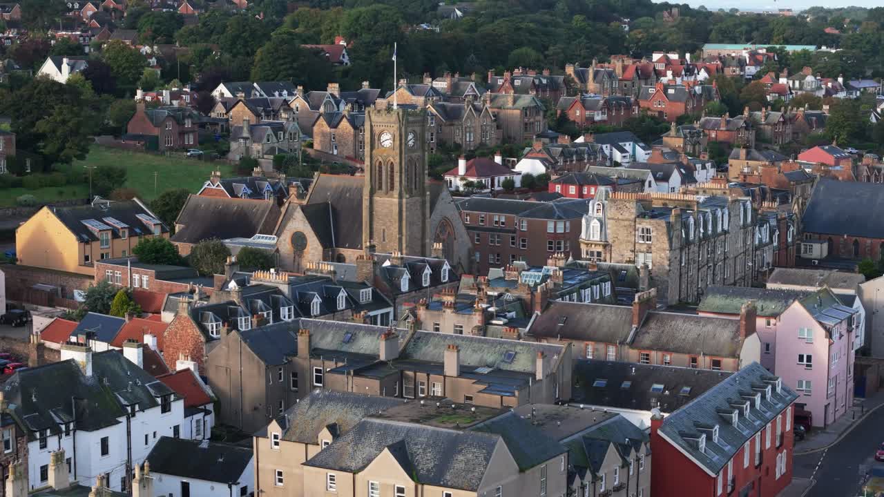 Aerial drone footage captures North Berwick, Scotland, in morning sunlight. views of the town’s historic church and town center