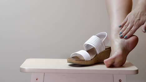 woman rubs oil all over foot as she traces lines up leg in front of white cork heels on stool