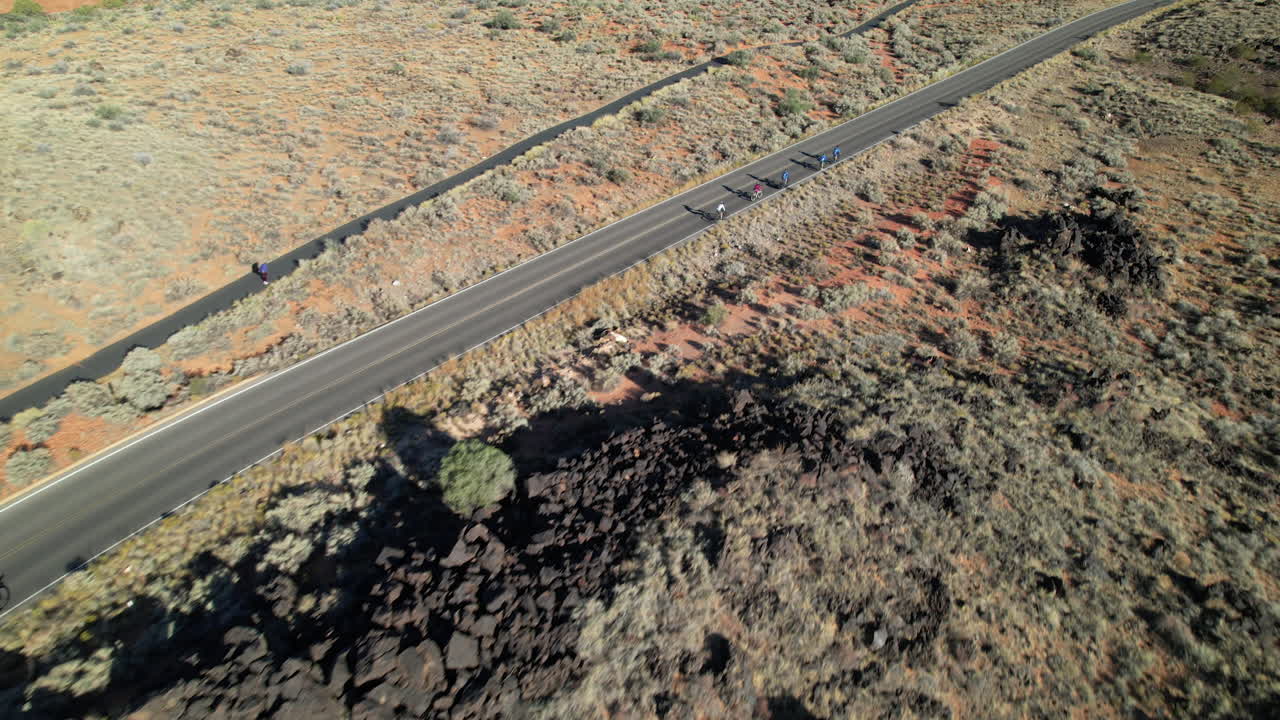 Overhead drone shot tracking a group of cyclists climbing a scenic road through Snow Canyon's rugged desert landscape.