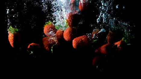 strawberries dropped into water on black background, slow motion close up