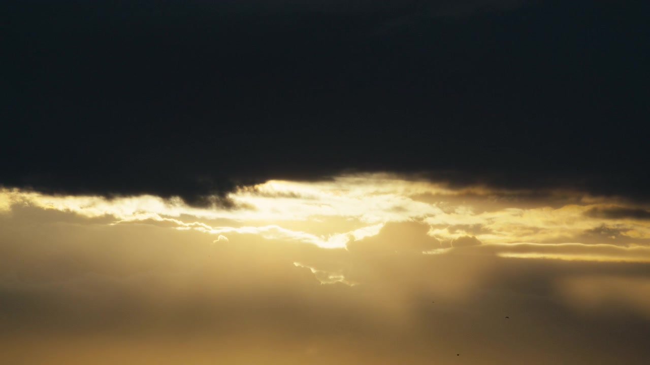 Bright evening sun streams through a low storm shelf, sending soft beams across the horizon in a calm Norwegian sky.